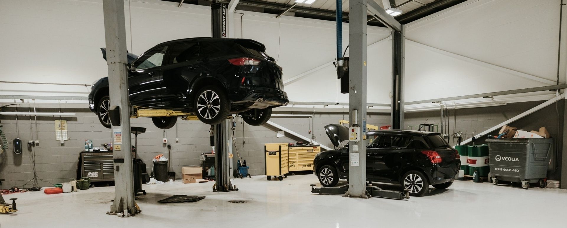 2 Black Cars On Lifts In a Workshop